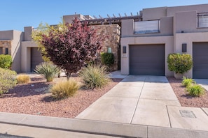 A modern building with a stone facade, a garage, and a well-maintained garden with various shrubs and a tree.