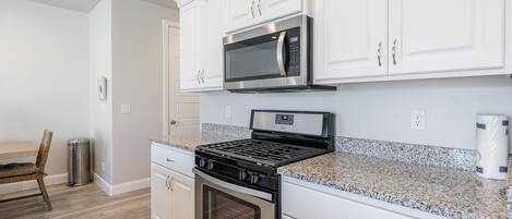 A kitchen with white cabinets, a stainless steel stove, a microwave, and a granite countertop.