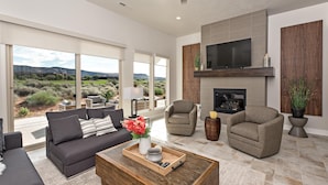 A spacious living room with a large window, a fireplace, and a flat-screen TV. - Villa On The 18th (St. George)
