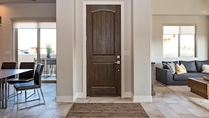 A modern living room with a dark wooden door, a dining area with a table and chairs, and a grey sofa with cushions. - Villa On The 18th (St. George)