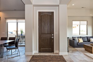 Un salon moderne avec une porte en bois foncé, un coin repas comprenant une table et des chaises, et un canapé gris agrémenté de coussins.