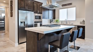 A modern kitchen with dark wood cabinets, stainless steel appliances, a central island with bar stools, and a large window. - Villa On The 18th (St. George)