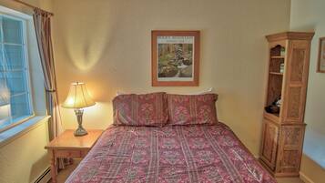 A bedroom with a bed, a nightstand with a lamp, a wooden cabinet, and a framed picture of Rocky Mountain National Park on the wall.