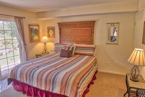 A bedroom with a large bed, a window with curtains, a bedside table with a lamp, and a mirror on the wall. - Villas at Swan's Nest #701 (Condo) Apartment 2 (Breckenridge)