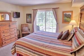 A bedroom with a large bed, a dresser, a chair, a television, and a window with curtains. - Villas at Swan's Nest #701 (Condo) Apartment 2 (Breckenridge)