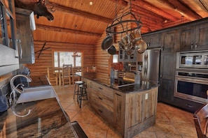 Una cocina rústica con paredes de madera, una isla central, electrodomésticos de acero inoxidable y ollas colgantes.