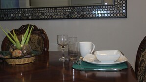 A dining table with a glass vase, two wine glasses, a white cup, a white bowl, and a green placemat. - Ladyville 2Bed 2Bath (Ladyville)