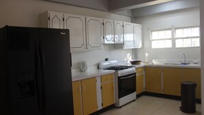 A kitchen with a black refrigerator, white and yellow cabinets, a stove, and a sink. - Ladyville 2Bed 2Bath (Ladyville)