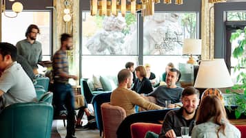 Una cafetería moderna con paneles de techo de madera, lámparas colgantes y un amplio ventanal con vistas a zonas verdes.