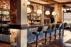 A bar area with a brick wall, shelves of bottles, and leather bar stools. - The Hoxton, Portland (Portland)