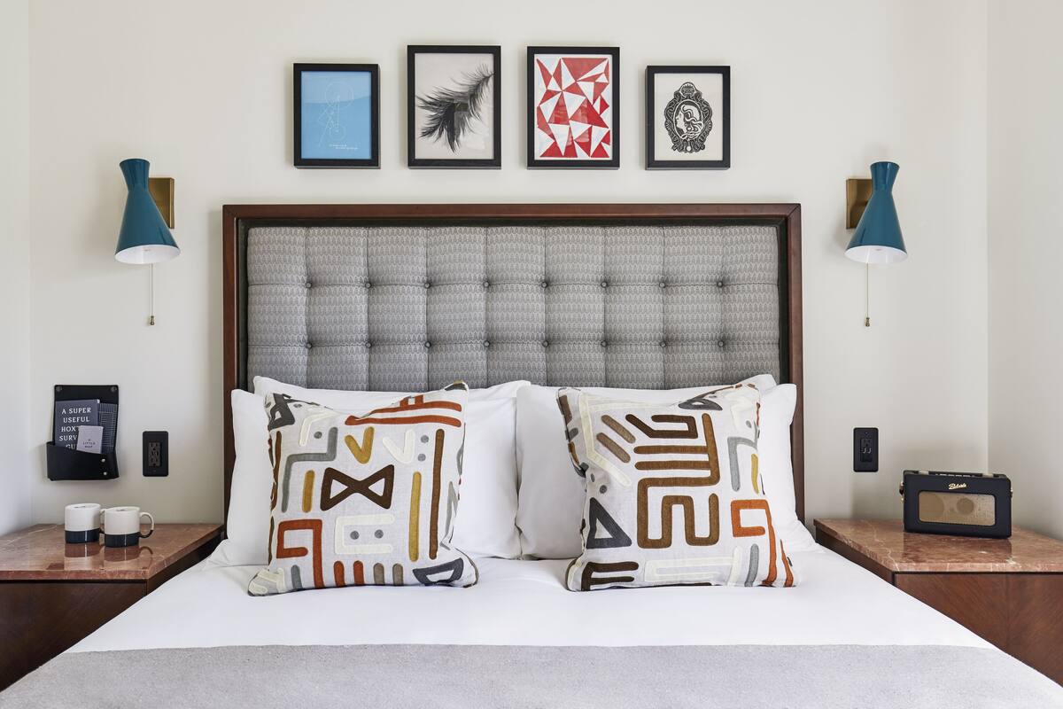 A neatly made bed with patterned pillows, a headboard with tufting, and framed artwork above.