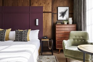 Habitación de hotel con cama, mesita de noche, cómoda, silla y mesa redonda.