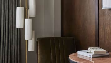 A hotel room with a round table, a gold floor lamp, a green upholstered chair, and a bed with white bedding.