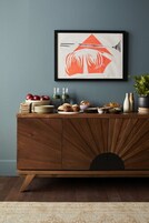 Un mueble de madera con un panel frontal decorativo, una obra de arte enmarcada encima y varios artículos de comida en la repisa superior.