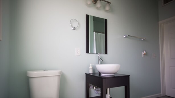 A bathroom with a toilet, a sink with a mirror, and a towel rack. - Wanderstay Houston Hostel (Houston)