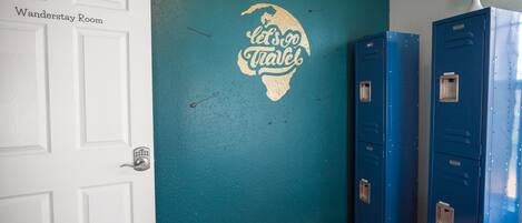A room with a teal wall, a white door labeled "Wanderstay Room," and blue lockers.