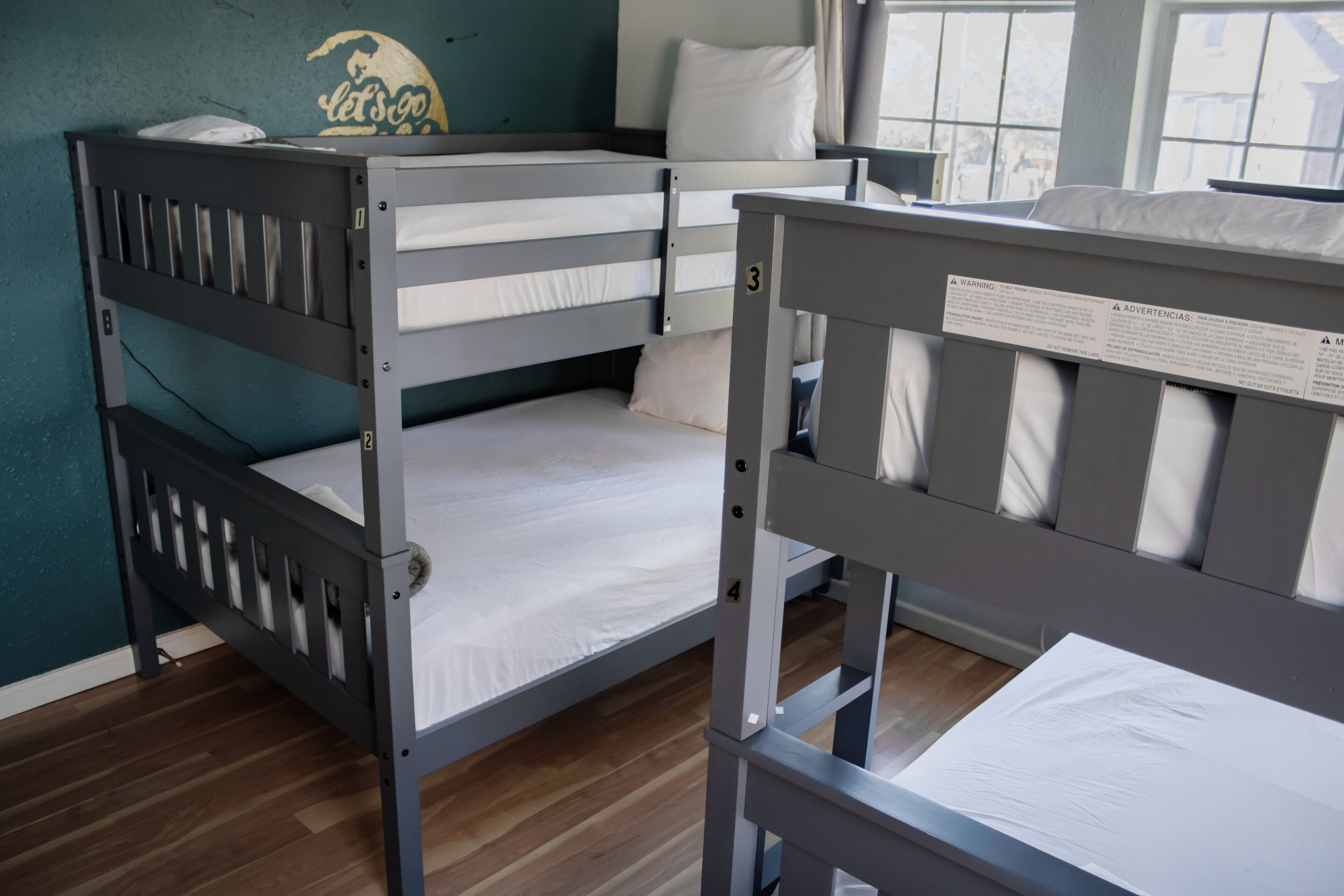 Dormitorio con literas, pared verde azulada, ventana y suelo de madera.