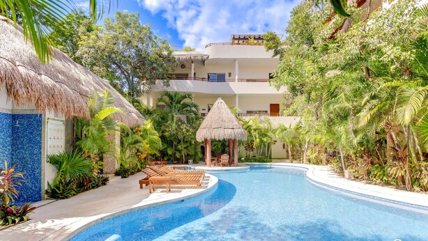 Uma piscina com design curvo, rodeada por vegetação exuberante e uma estrutura com telhado de palha.