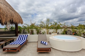 A rooftop lounge area with two sun loungers, a hot tub, and a thatched roof structure. - Condo Complex with an Alluring Pool & Tropical Vibes by Stella Rentals (Tulum)