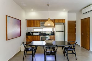 A modern kitchen with wooden cabinets, a stainless steel refrigerator, and a dining area with a black table and chairs. - Condo Complex with an Alluring Pool & Tropical Vibes by Stella Rentals (Tulum)