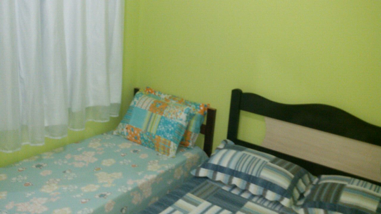 A small bed with floral bedding and striped pillows, a wooden headboard, and a green wall.
