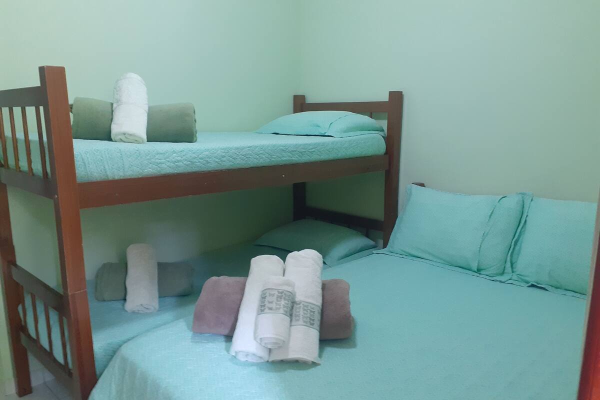 Ein Schlafraum mit Etagenbetten, einer grünen Tagesdecke, Kissen und aufgerollten Handtüchern.