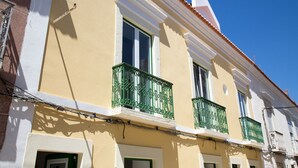 Un edificio amarillo con detalles blancos, balcones verdes y ventanas con marco blanco.
