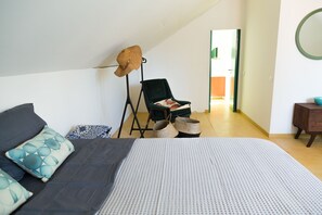 Et soveværelse med seng, stol, hatteholder og et lille bord.