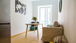 Un espacio habitable compacto con kitchenette, un sofá, una mesita y una planta decorativa.