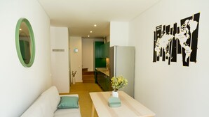 Un salón moderno con un sofá blanco, una mesita con un jarrón de flores y un espejo con marco verde. Un mapa del mundo está colgado en la pared.