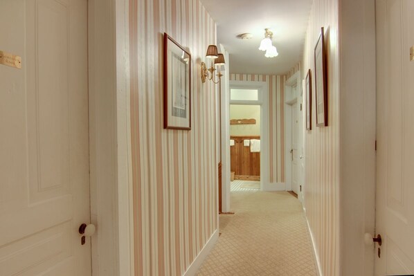 A hallway with striped wallpaper, framed pictures, and a light fixture. - The Park Street Inn (Bellaire)