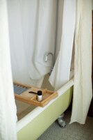 Un baño con una bañera verde, una bandeja de madera con una botella y una cortina de ducha.