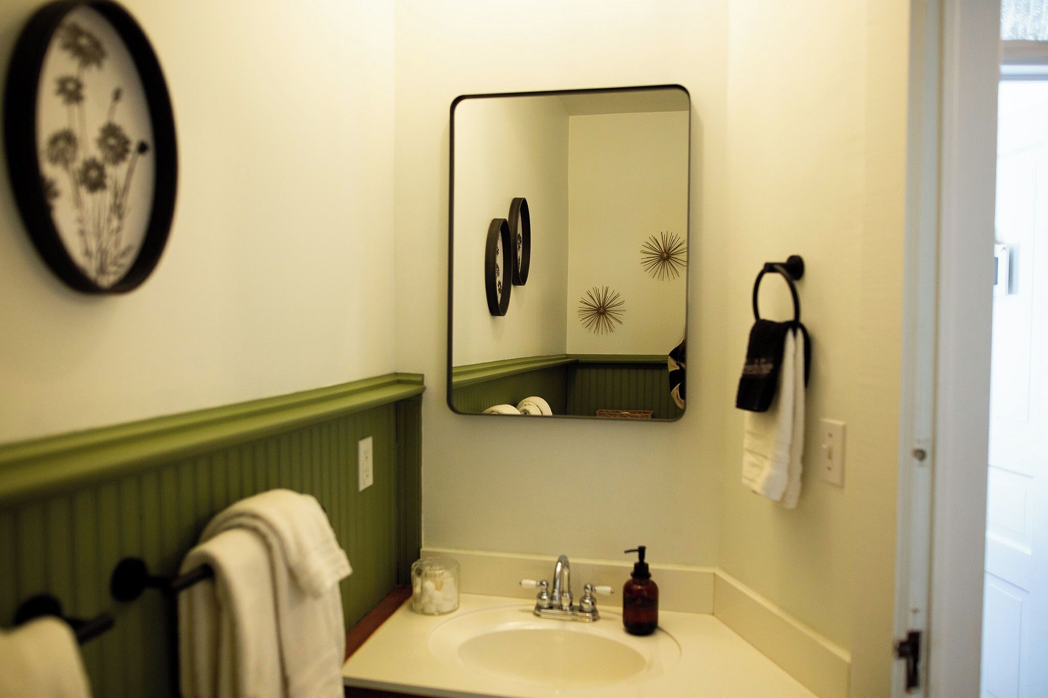 Une salle de bain équipée d’un lavabo, d’un miroir, d’un porte-serviettes et d’un élément décoratif fixé au mur.
