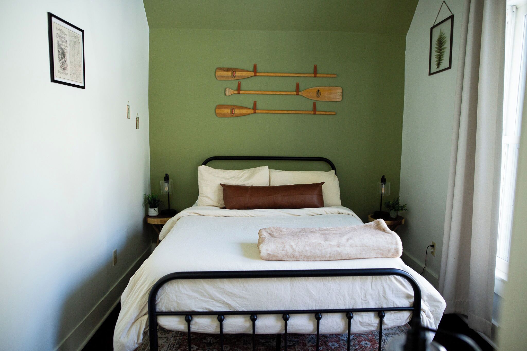 Ein schmales Zimmer mit einem Bett, einer grünen Wand und hängenden Holzschlägern.