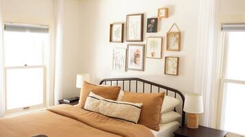 Un dormitorio con cama, mesitas de noche, una obra de arte en la pared y una lámpara en el techo.