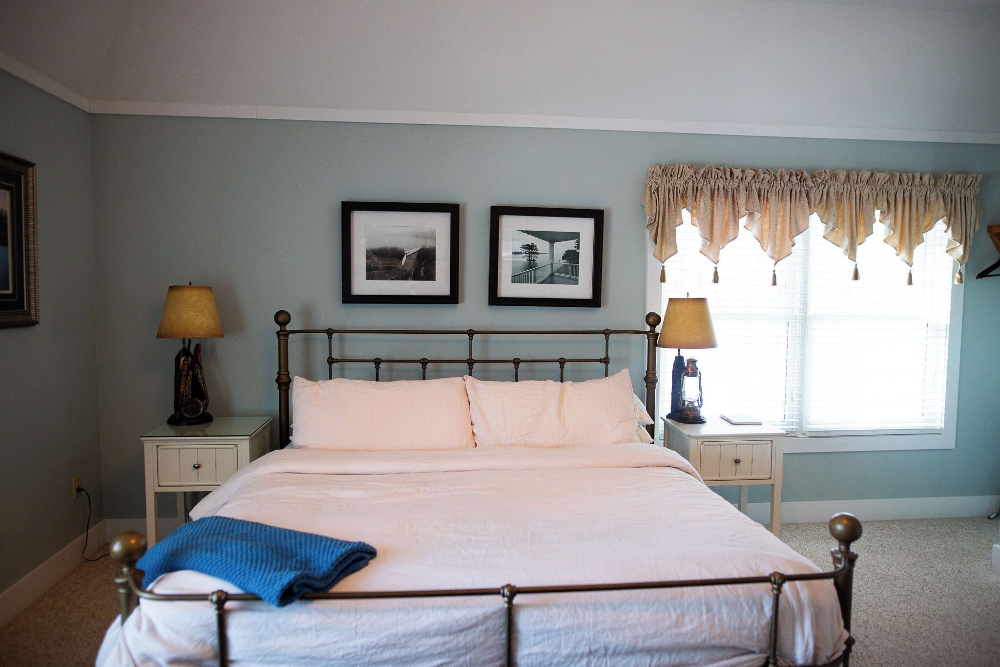 A neatly made bed with white linens, two bedside tables with lamps, and framed pictures on the wall.