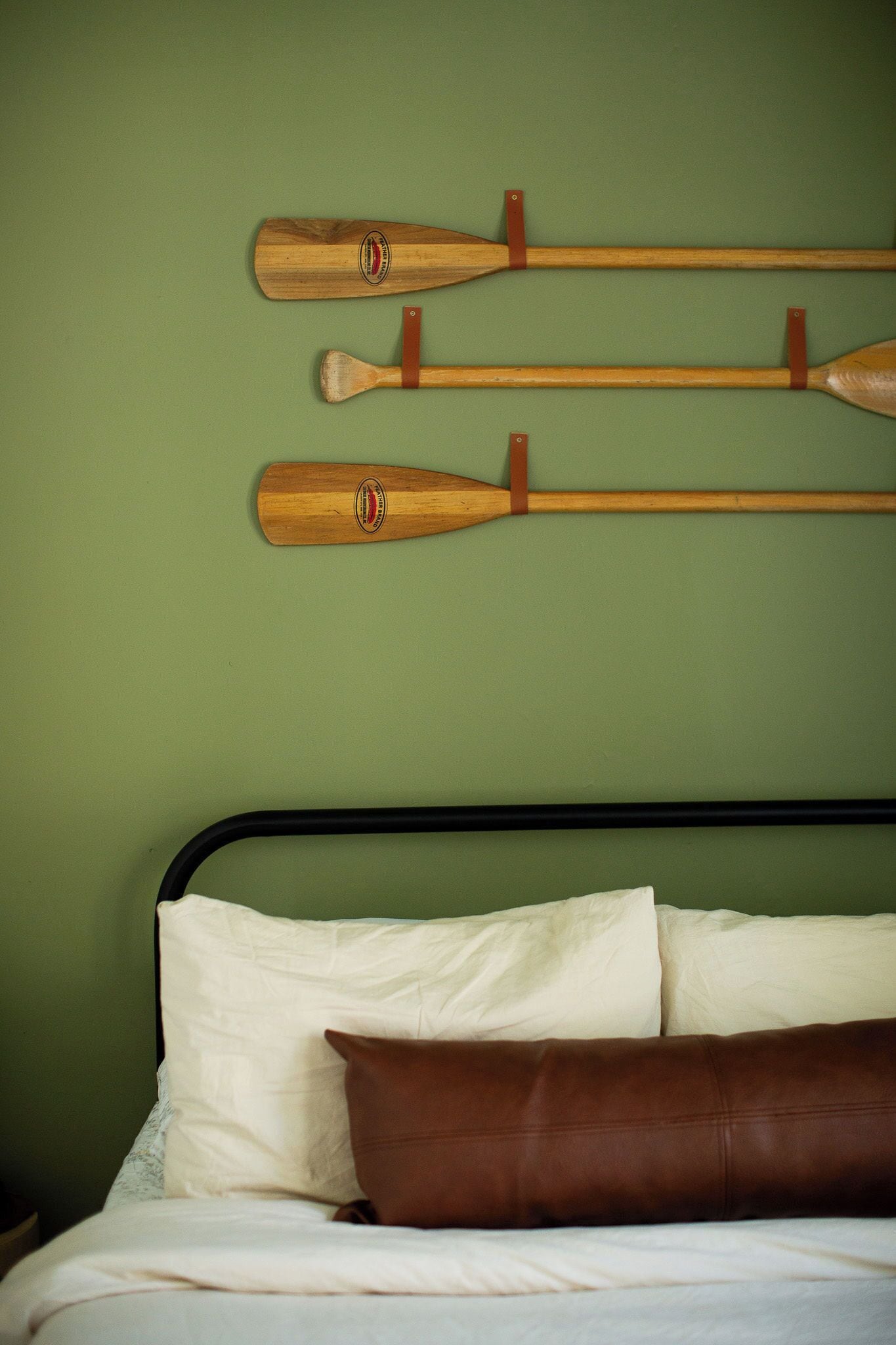 A bed with white and brown pillows, a green wall, and wooden paddles hanging on the wall.