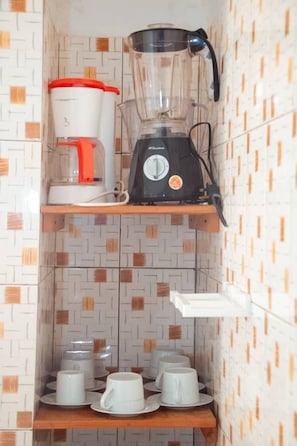 A kitchen with a blender and coffee maker on a shelf, and several cups on a lower shelf.