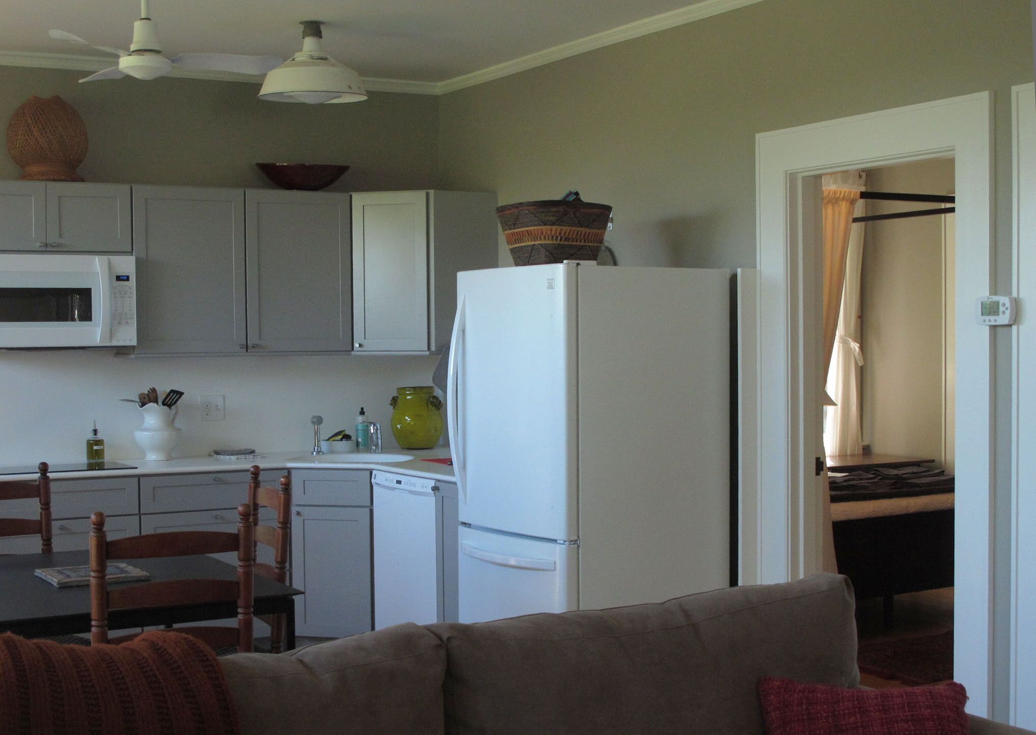 A compact kitchen with white cabinets, a microwave, and a refrigerator. There is a dining table with chairs and a sofa in the living area.