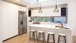 A modern kitchen with white cabinetry, a stainless steel refrigerator, a gas stove, and a large island with bar stools. - Superb Dual Keyed Home with Stunning Ocean Views just 300 Metres to Beach (Dunsborough)