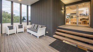 A modern outdoor deck with a sofa and chairs, wooden steps leading to a glass door, and a view of the interior. - Superb Dual Keyed Home with Stunning Ocean Views just 300 Metres to Beach (Dunsborough)