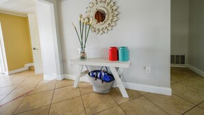 Un pasillo con pared blanca, un espejo decorativo, un jarrón con flores y una mesa con dos botellas de agua.
