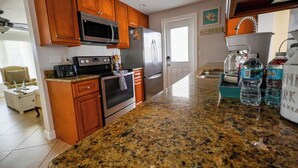 Cocina con armarios de madera, electrodomésticos de acero inoxidable y encimeras de granito, y un refrigerador con imanes.