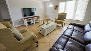 Una sala de estar con televisor, sofá, sillón, mesa de centro y ventilador de techo.