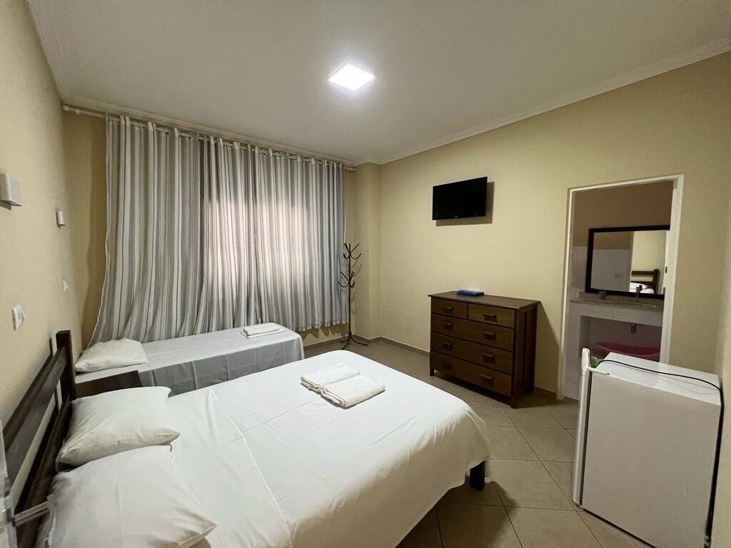 Ein Hotelzimmer mit zwei Betten, einem Fernseher, einem Schminktisch und einem Kühlschrank.