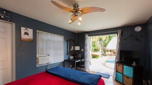 A bedroom with a red bed, a ceiling fan, a desk, a TV, and a view of the outdoors. - Clothes optional Tranquil Private room Paradise. In Fort Lauderdale. LGBTQ+ ❤️ (Oakland Park)