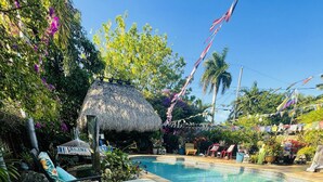 A pool area with lounge chairs, a thatched umbrella, and tropical plants. - Clothes optional Tranquil Private room Paradise. In Fort Lauderdale. LGBTQ+ ❤️ (Oakland Park)