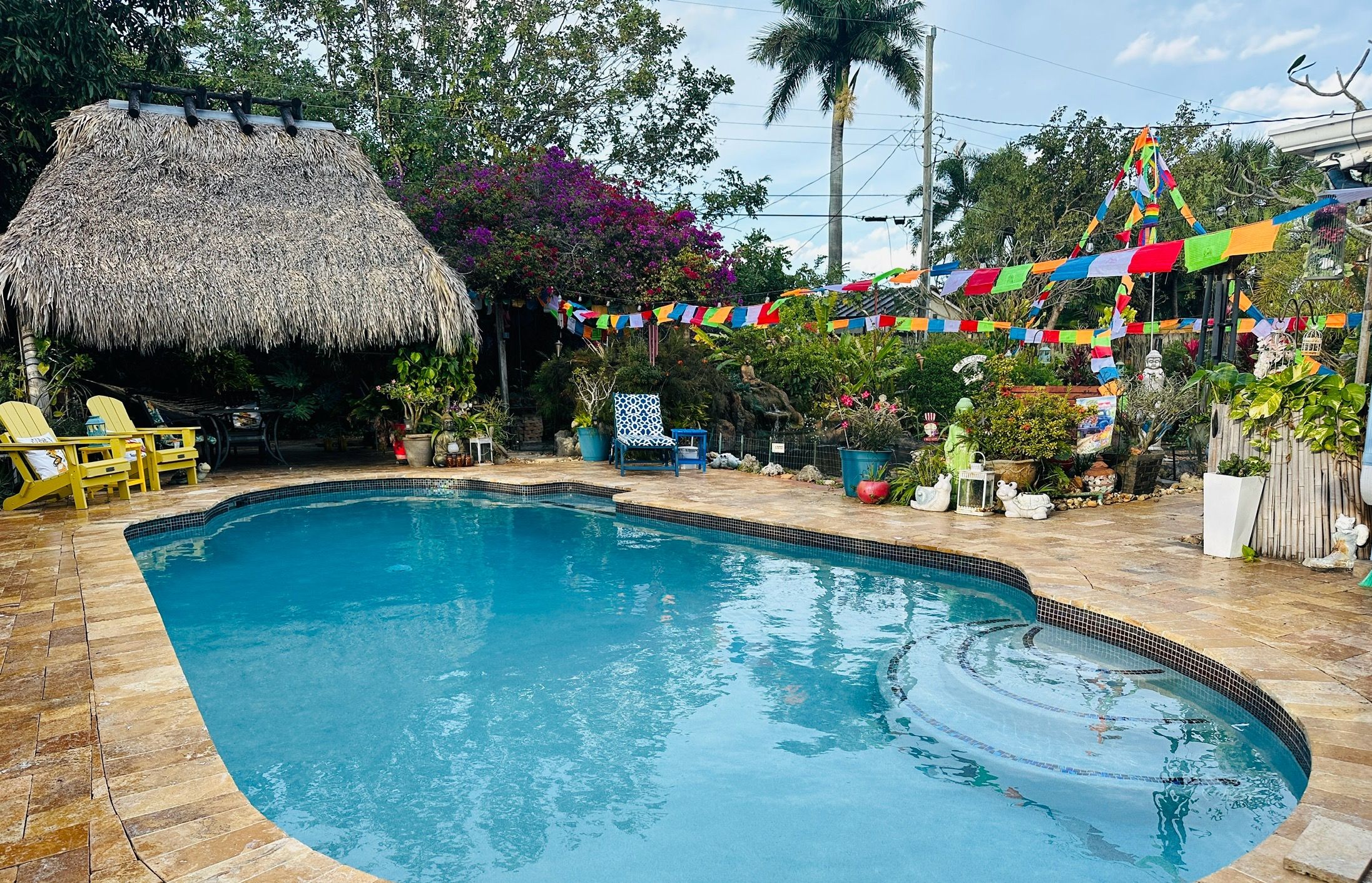 A swimming pool with a thatched roof structure and colorful prayer flags in the background.