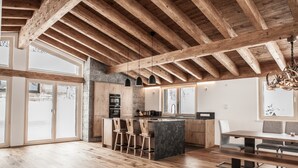 Una cocina amplia con vigas de madera, ventanas grandes y una isla central con taburetes de bar.