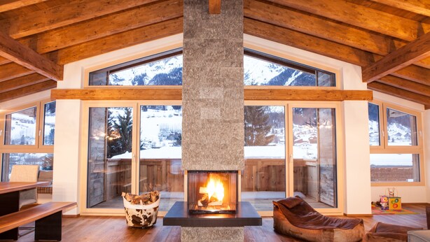 Amplia sala de estar con chimenea, vigas de madera, ventanas grandes y un rincón de asientos acogedor.